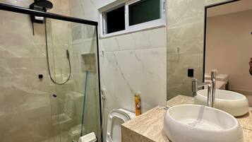 Een moderne badkamer met een douchecabine van glas, een toilet en een wastafel met twee wasbakken.