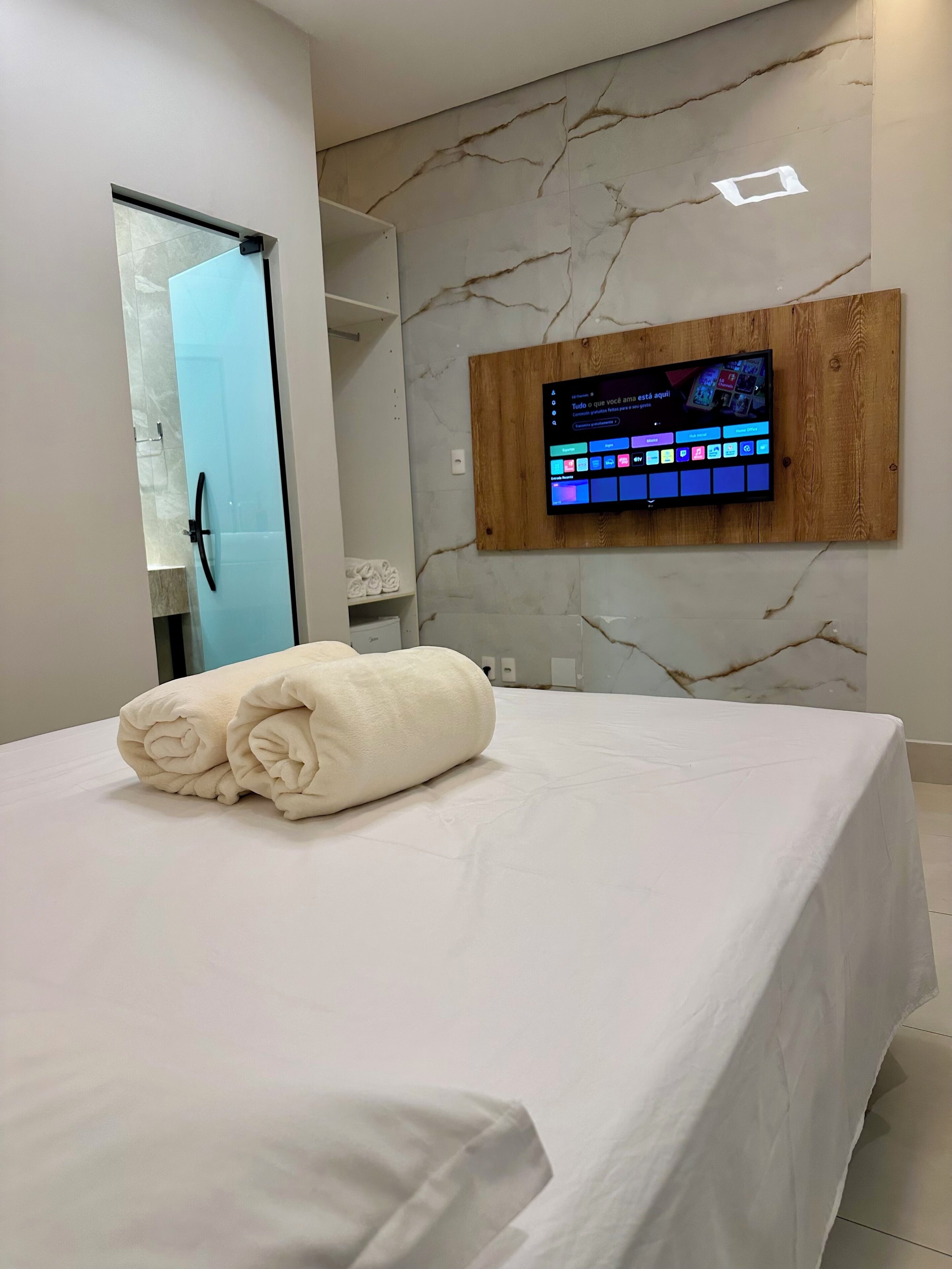 A hotel room with a bed, a wall-mounted TV, and a towel on the bed.