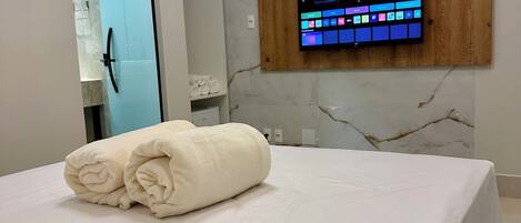 A hotel room with a bed, a wall-mounted TV, and a towel on the bed.