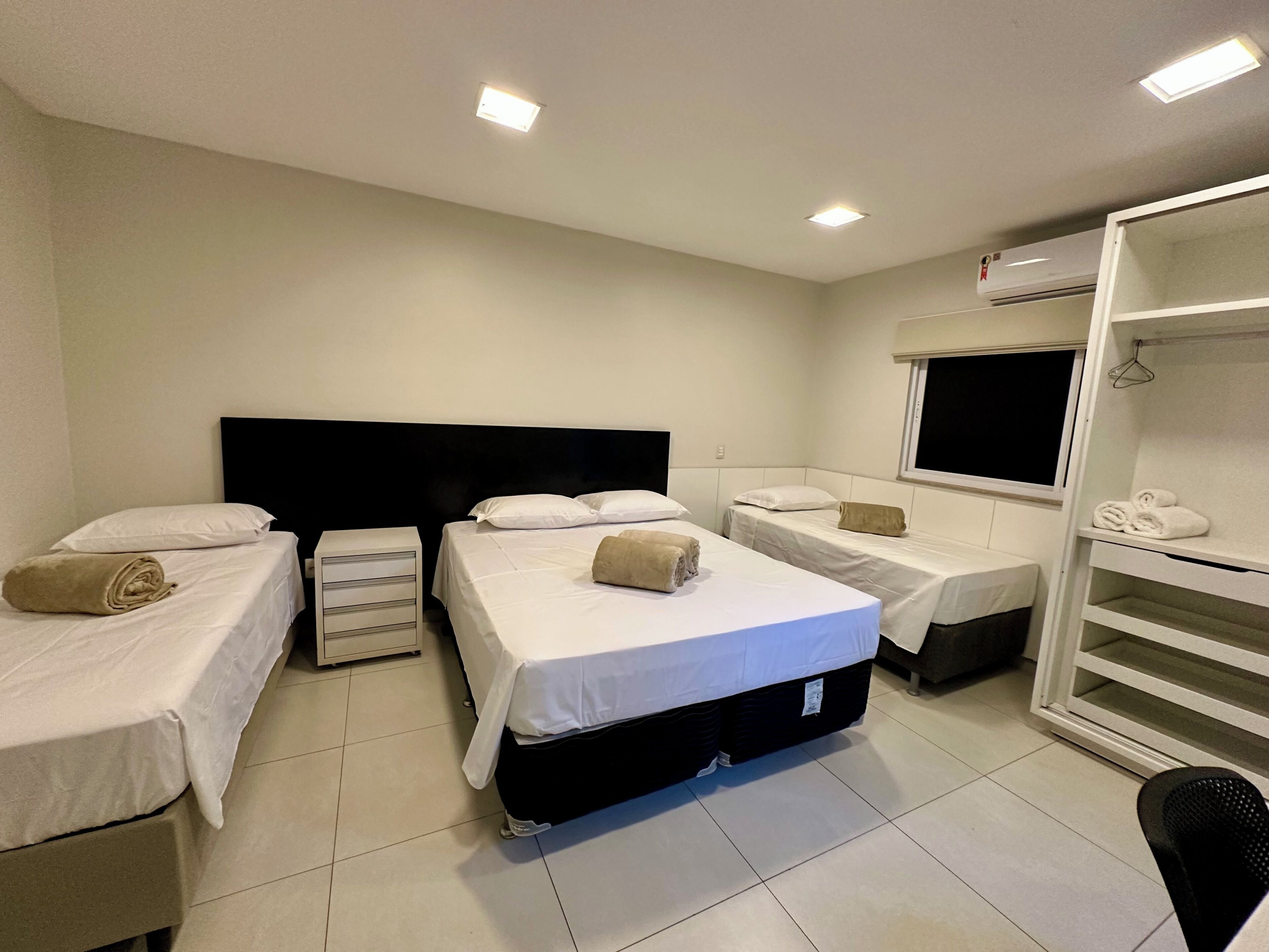 Une chambre d’hôtel avec trois lits simples, une armoire et une fenêtre.