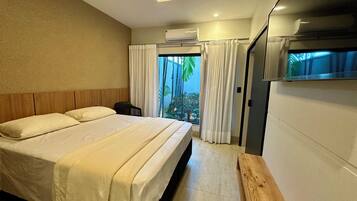 A hotel room with a bed, a small table, a window with curtains, and an air conditioning unit.