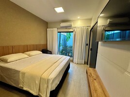 Quarto de hotel com cama, uma mesinha, janela com cortinas e ar condicionado.