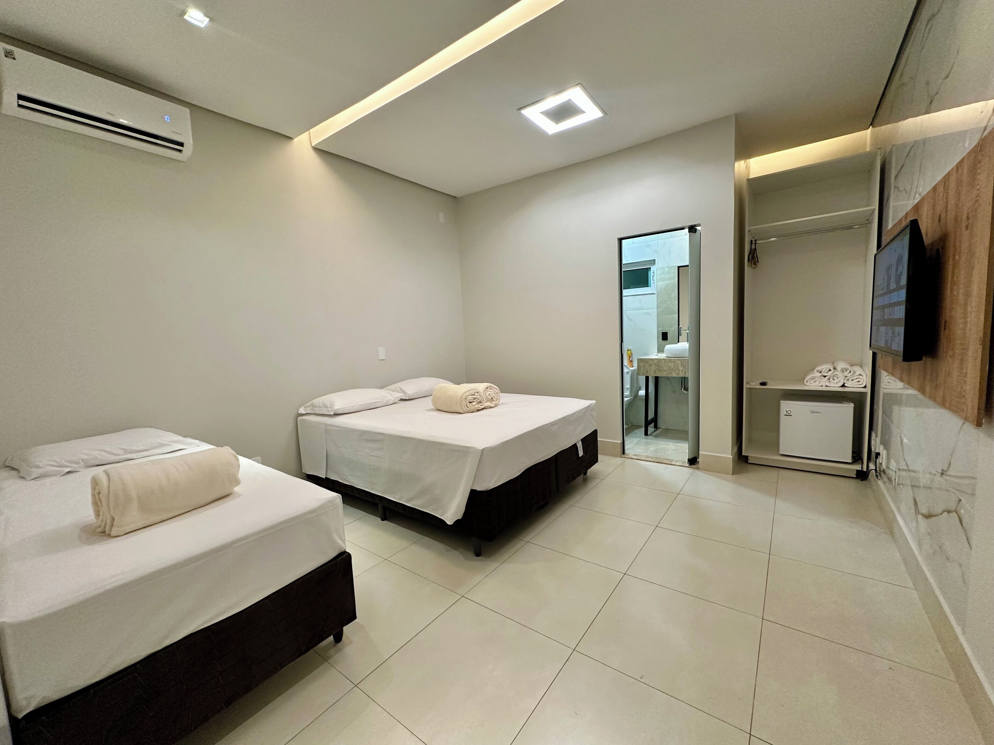 Habitación de hotel con dos camas, un kitchenette pequeño, un baño y un televisor montado en la pared.