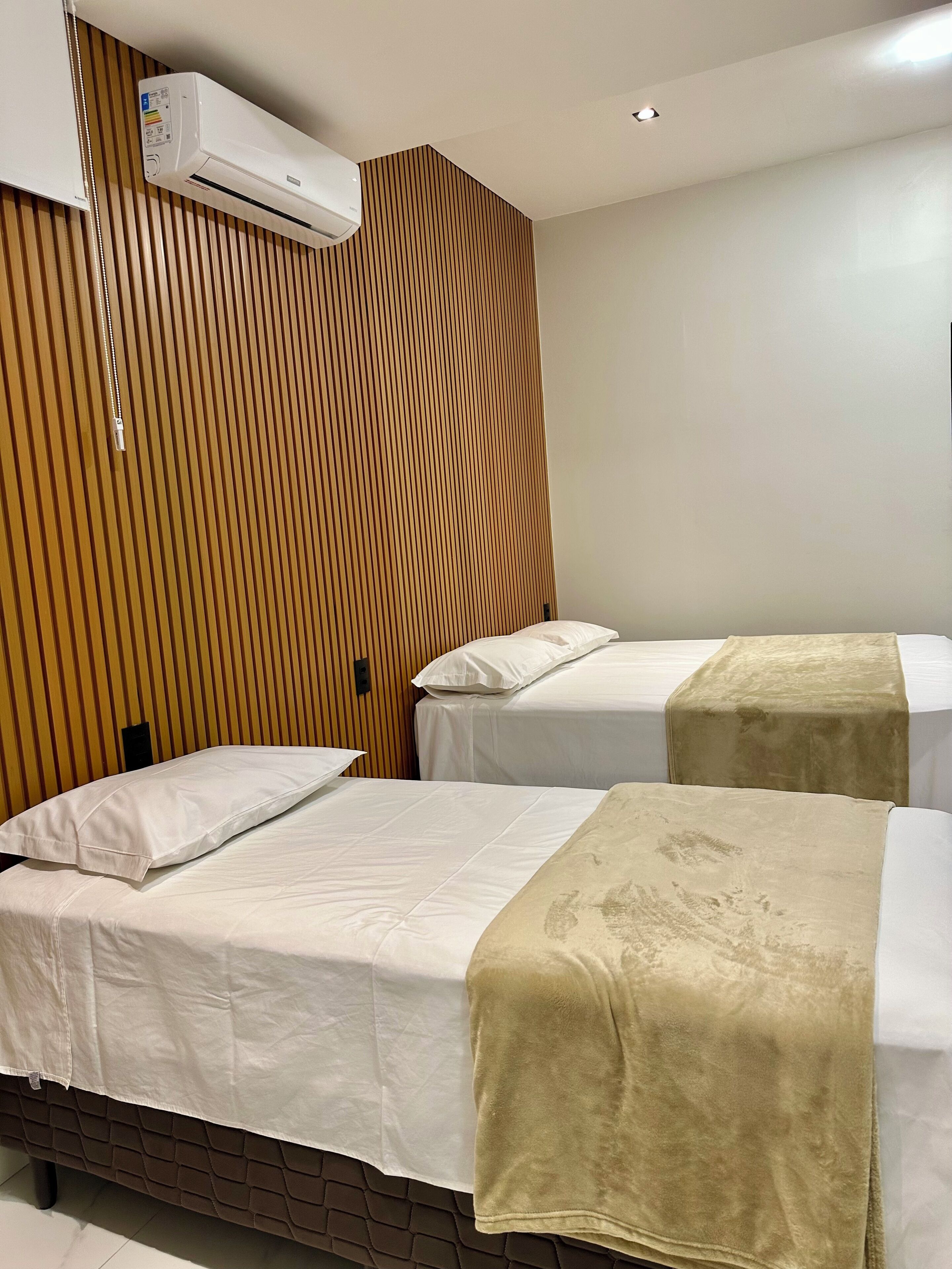 A hotel room with two beds, a wooden slat wall, an air conditioning unit, and a plain white ceiling.