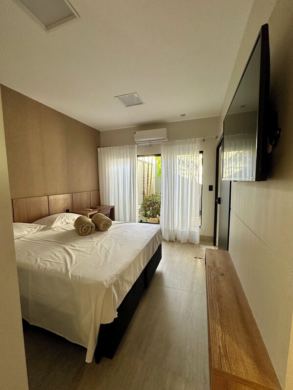 Ein Hotelzimmer mit Bett, Fernseher, Badezimmer und Blick auf Grünfläche.