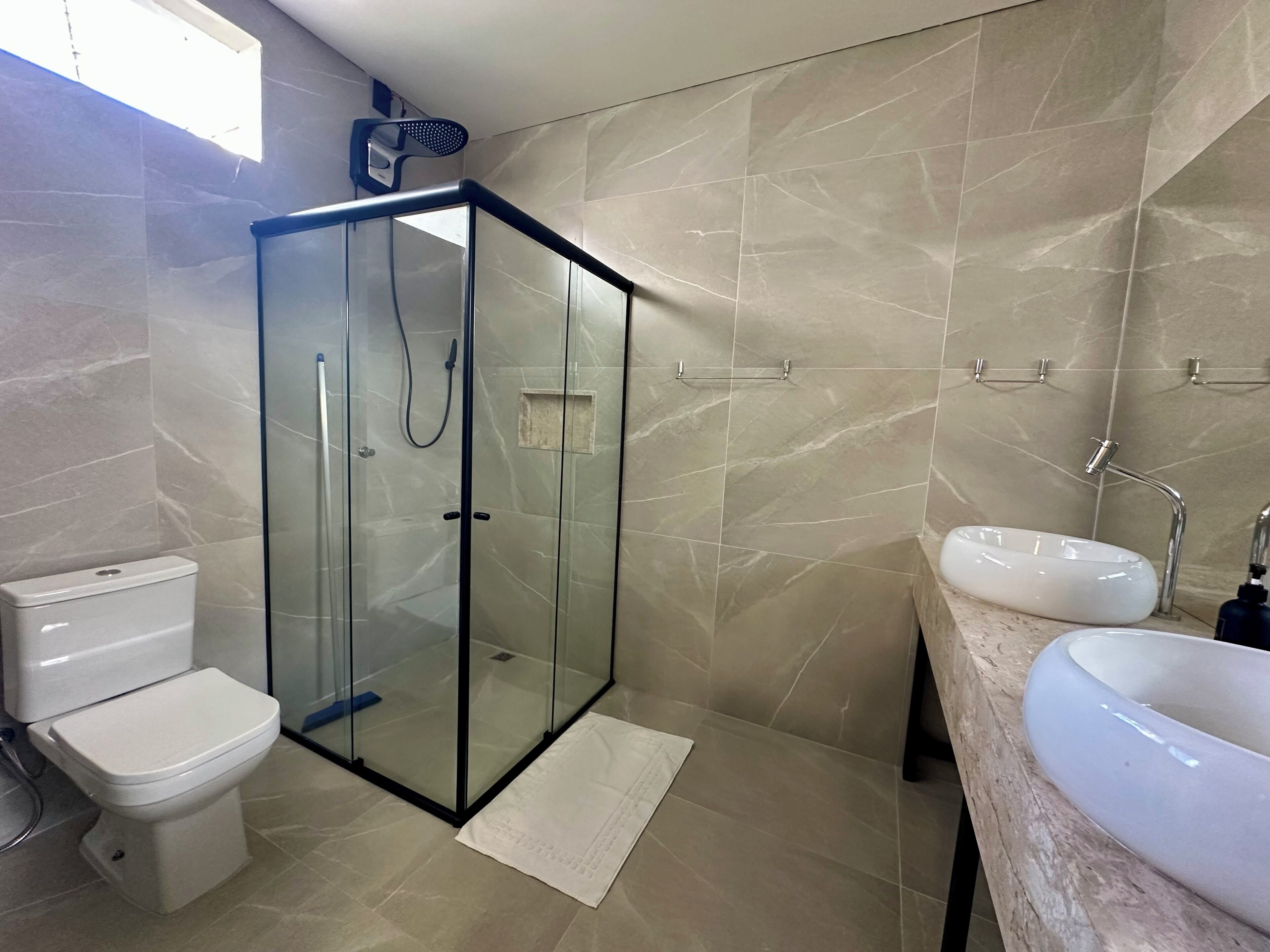 A bathroom with a glass-enclosed shower, a toilet, and a sink with a marble countertop.