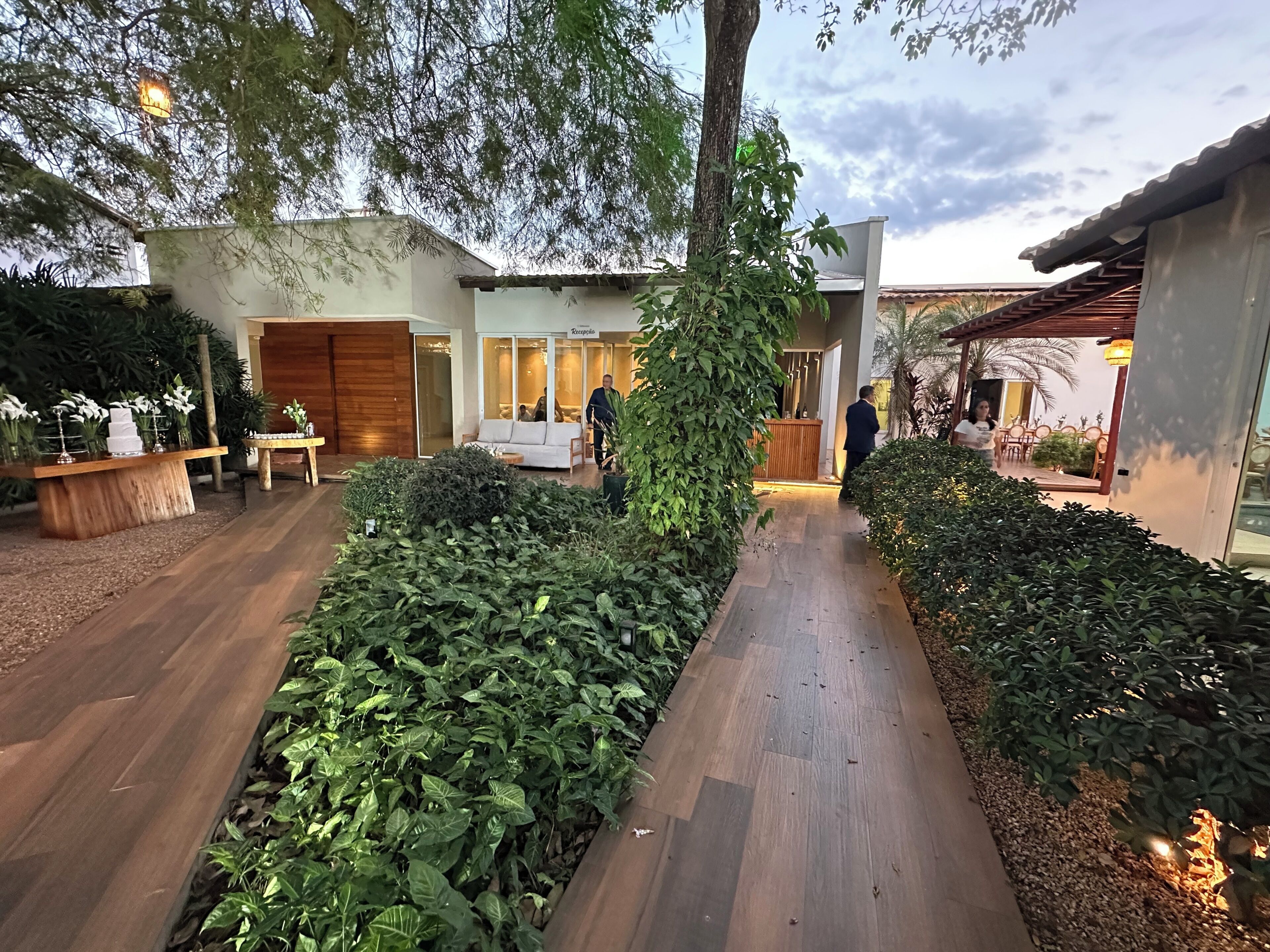 A modern outdoor area with a reception desk, seating, and a pathway lined with plants.