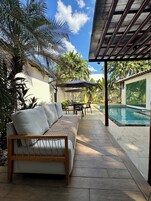 Un patio con piscina, mobiliario exterior y abundante vegetación.