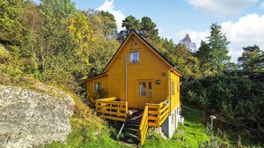 A yellow wooden cabin with a small porch and a single window, surrounded by lush greenery and trees. - Beautiful home in Reksteren with WiFi (Reksteren)
