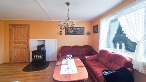 A cozy living room with a wooden table, a red sofa, a black heater, and a window with lace curtains. - Beautiful home in Reksteren with WiFi (Reksteren)