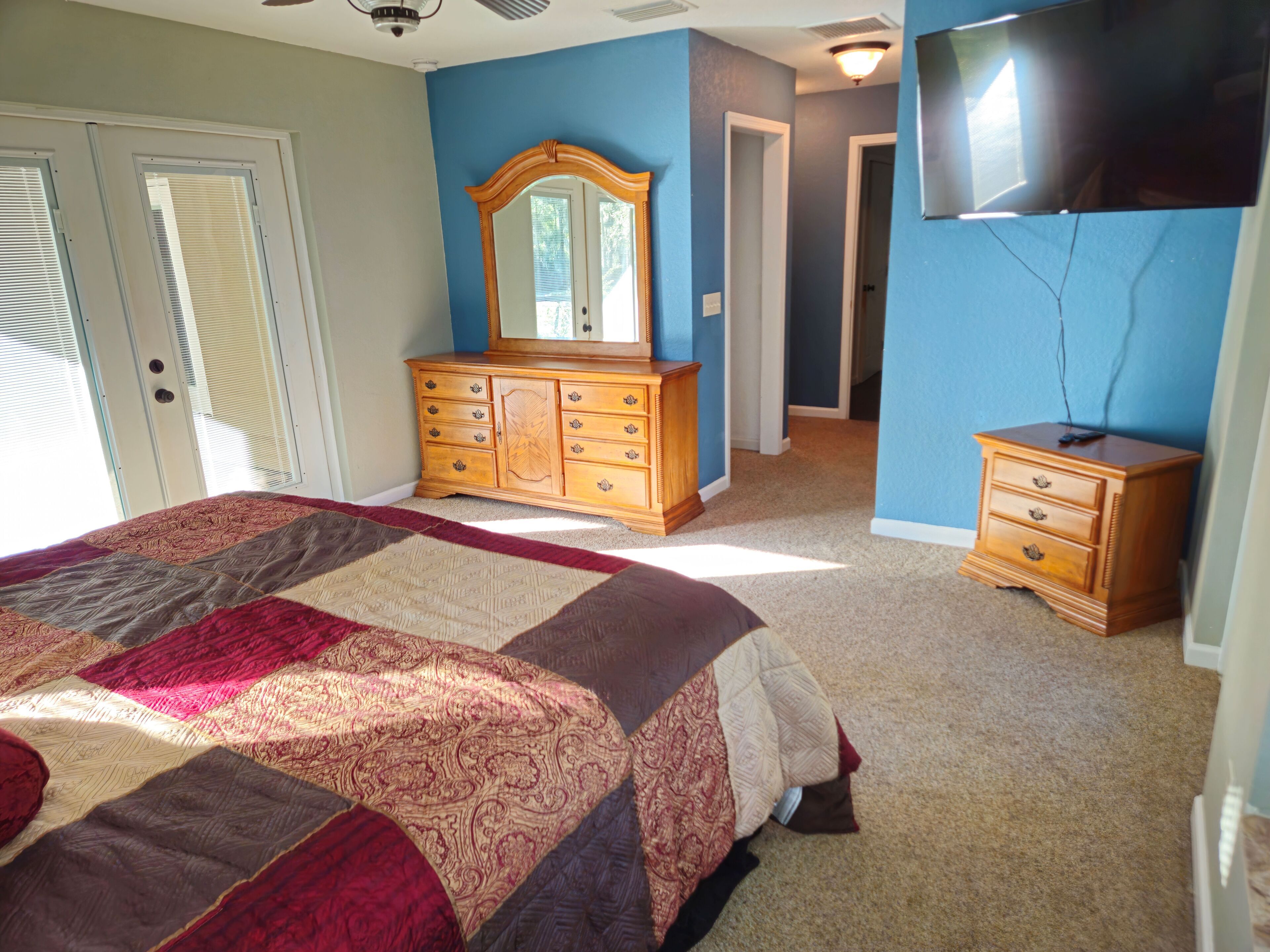 A bedroom with a large bed, a dresser, a mirror, and a television.