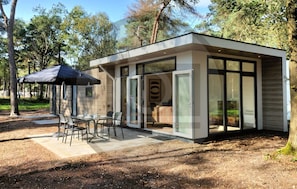 Un espace de restauration extérieur moderne, avec une table et des chaises, un parasol noir et une porte vitrée donnant accès à un bâtiment.