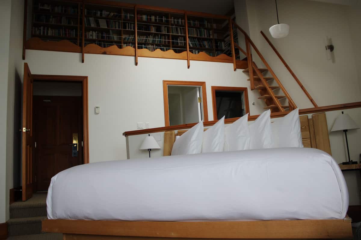 A hotel room with a large bed, a wooden staircase, and a bookshelf.