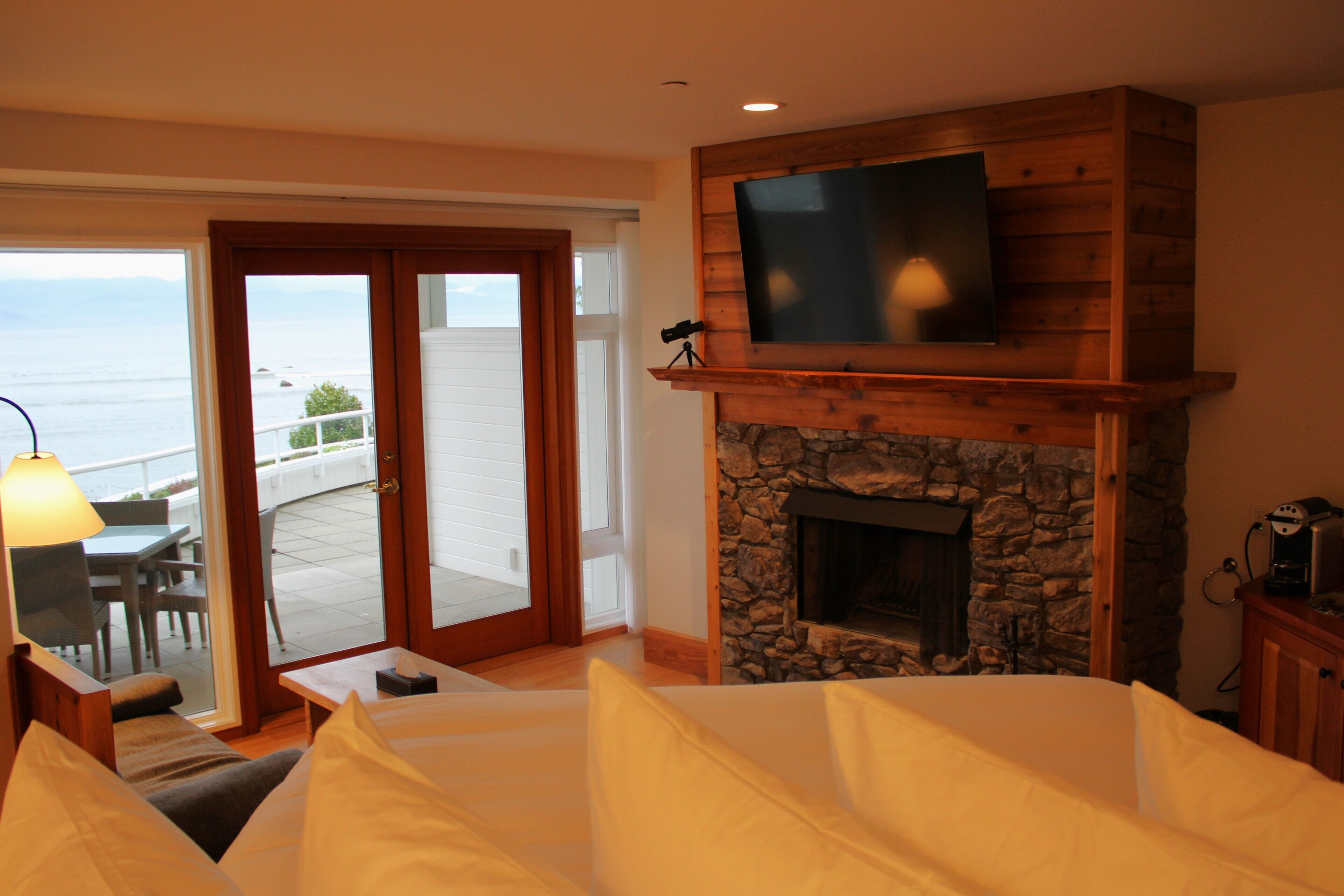 Une chambre d’hôtel avec une cheminée en pierre, un téléviseur fixé à un mur en bois et un balcon offrant une vue sur la mer.