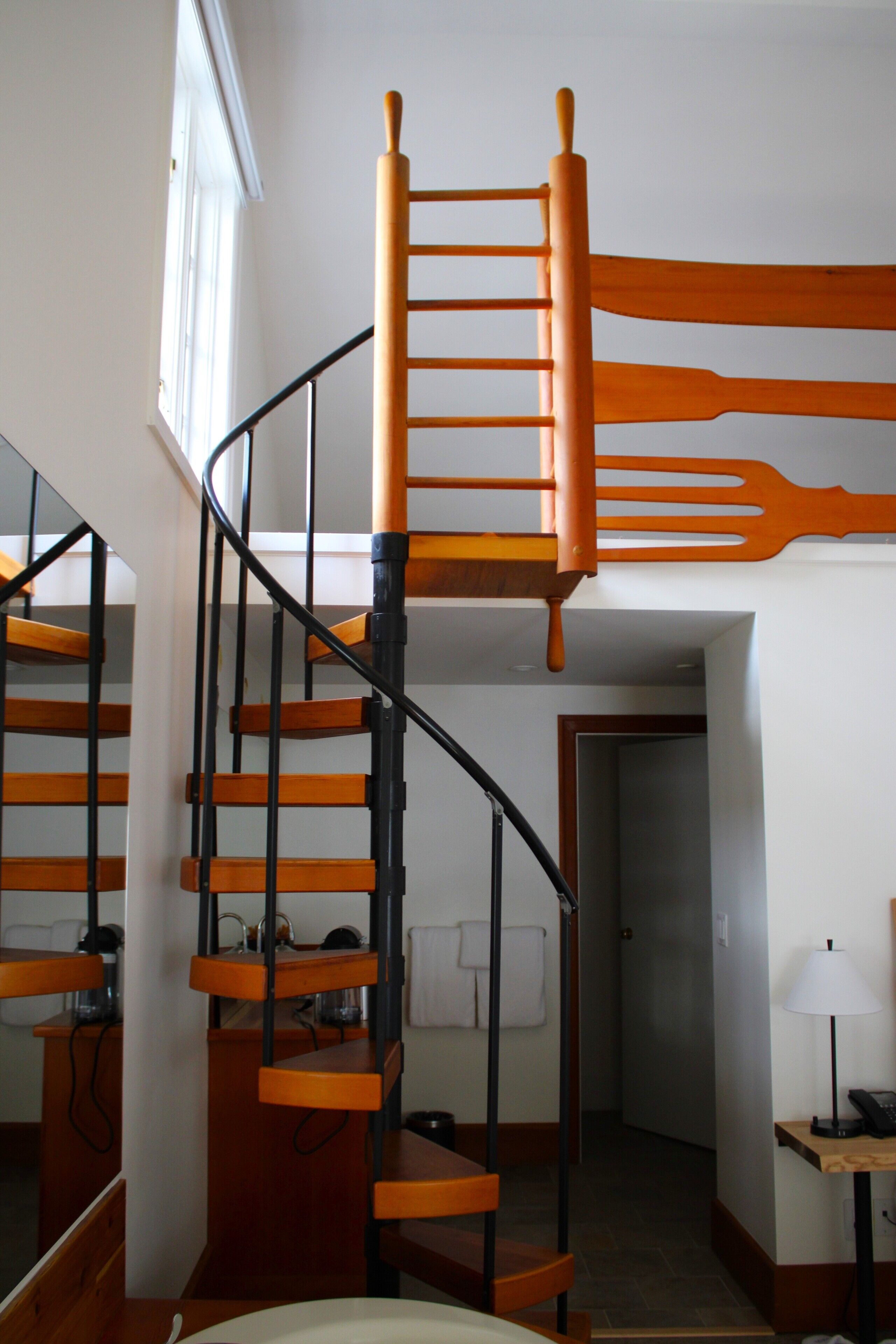 Una escalera en espiral con escalones de madera y barandillas negras, que conduce a un piso superior.