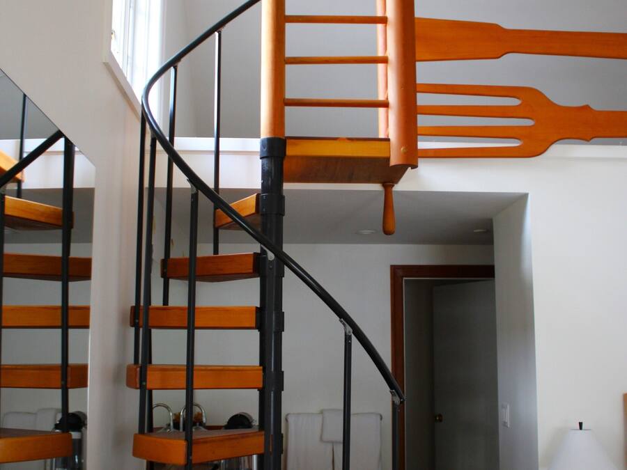 Una escalera en espiral con escalones de madera y barandillas negras, que conduce a un piso superior.