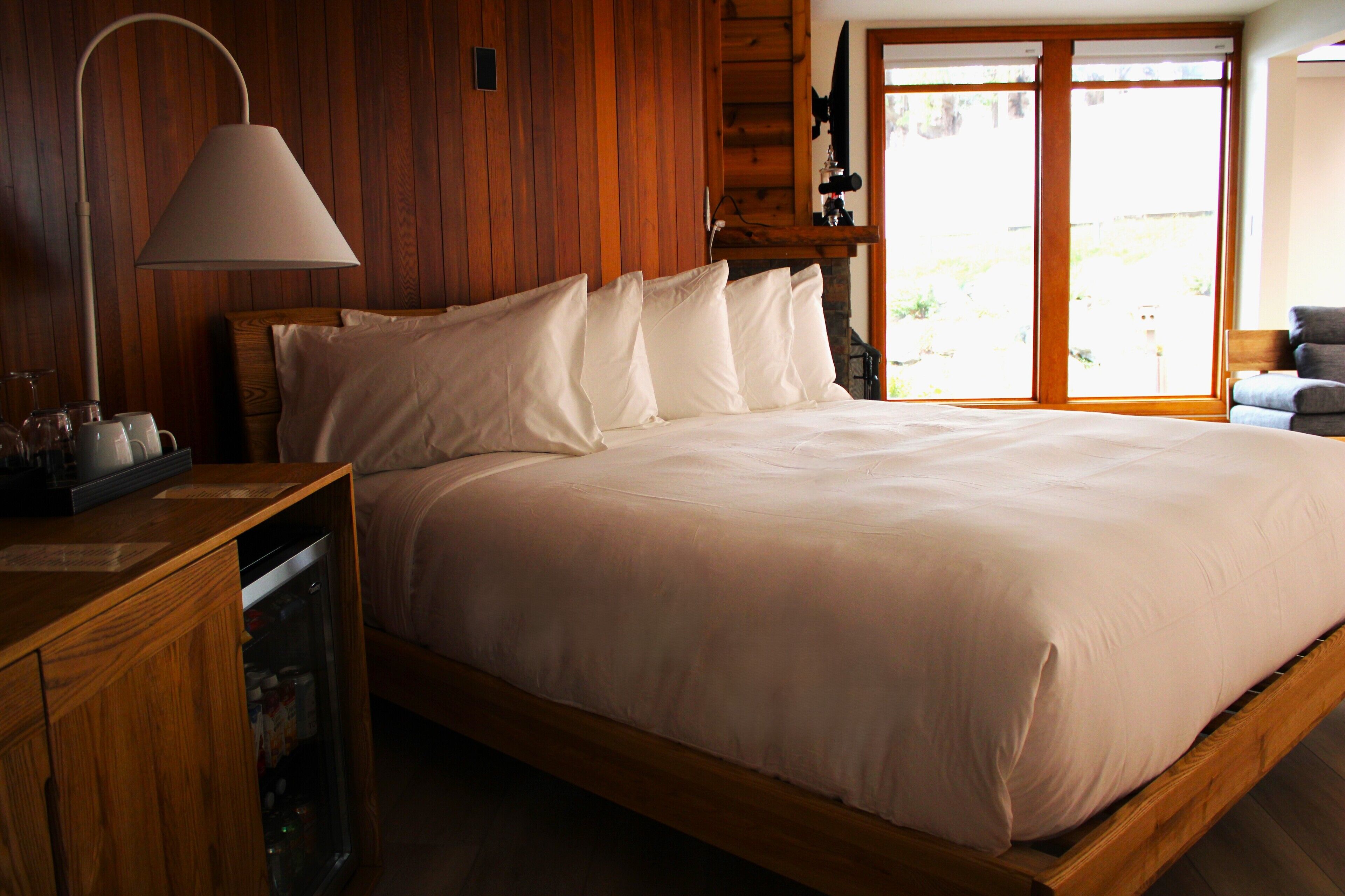 A wooden bed with white linens in a room with wooden walls and a large window.