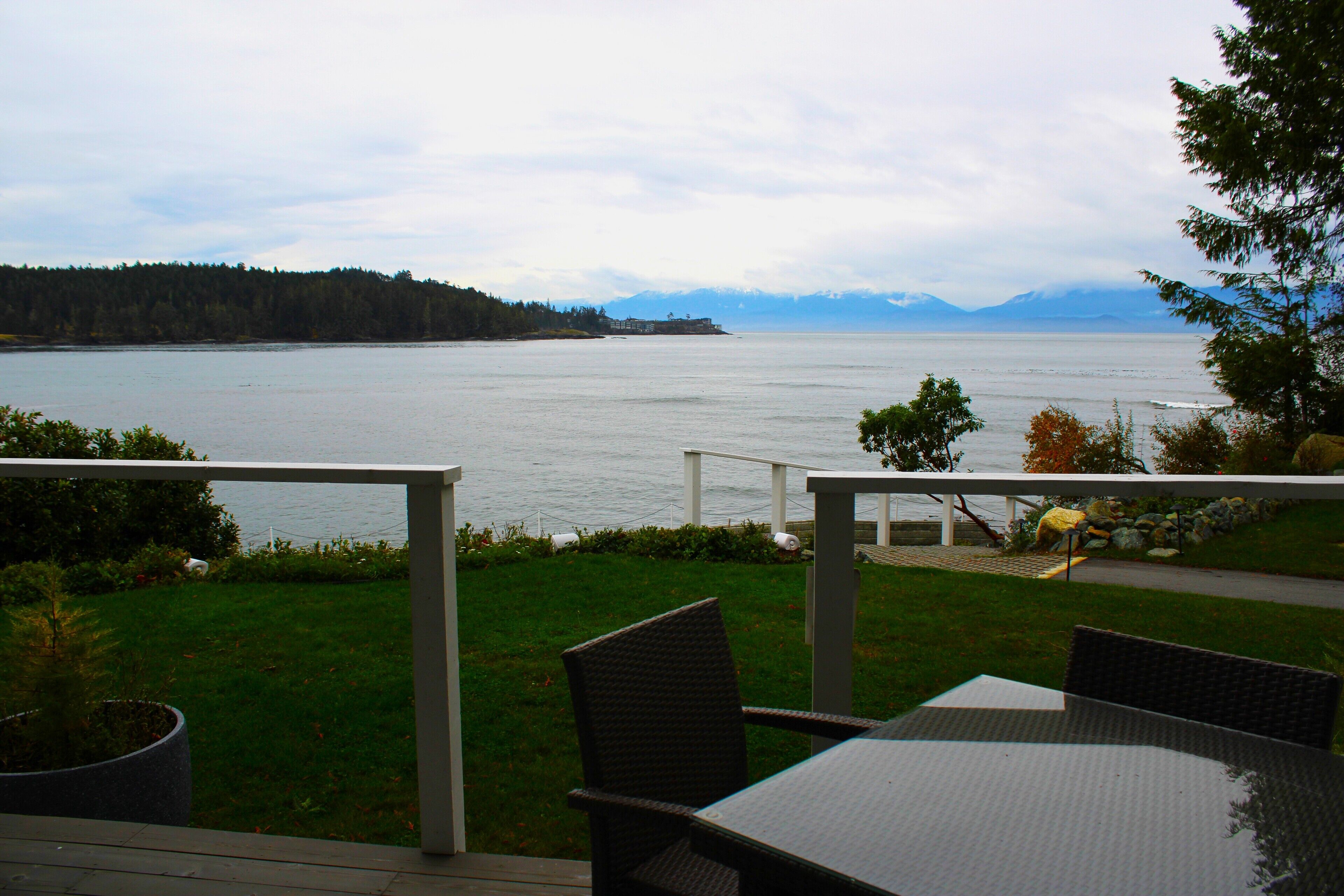 Un patio exterior con una mesa y sillas, con vistas a un lago tranquilo y montañas a lo lejos.