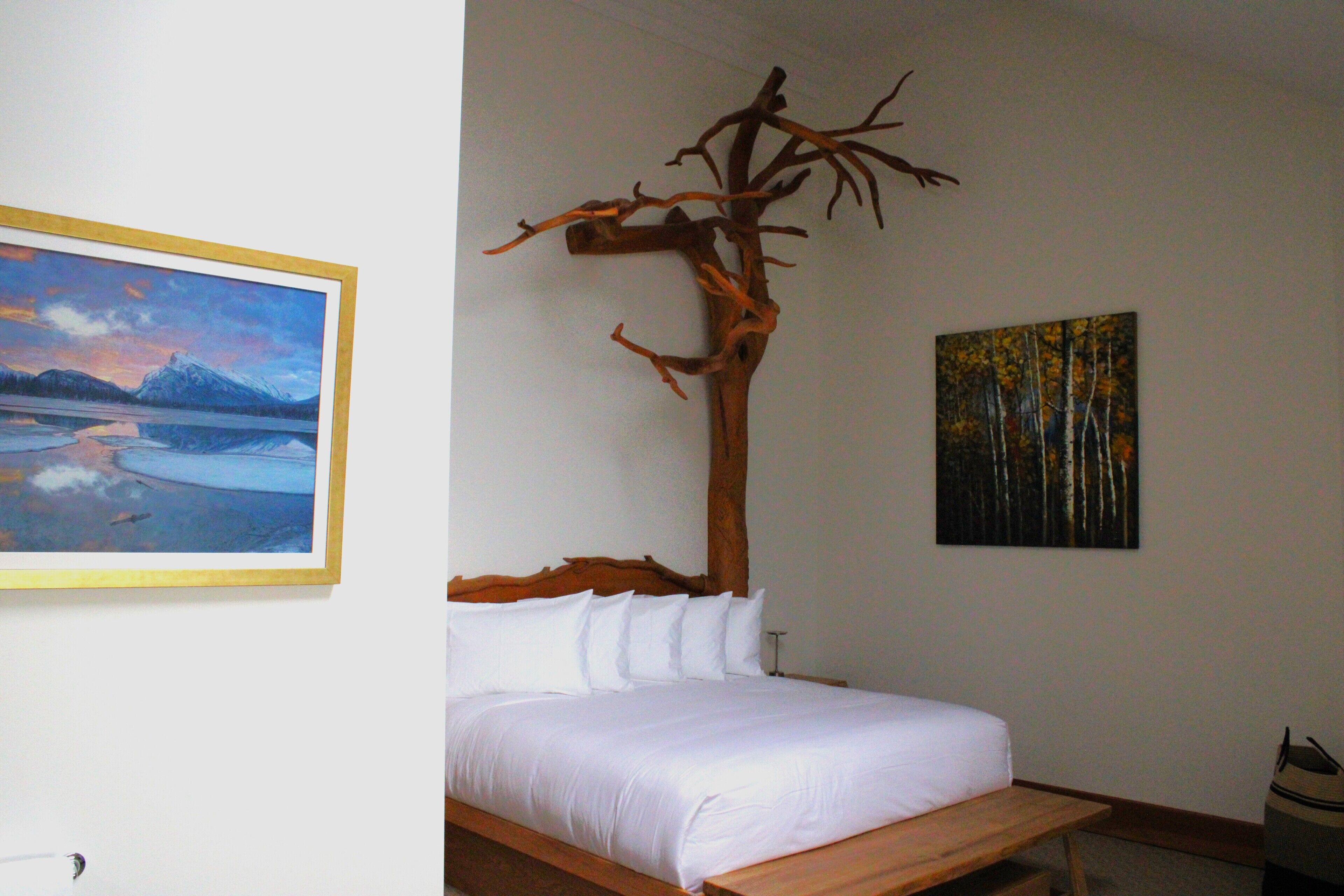 Een slaapkamer met een bed, een houten hoofdeinde en twee schilderijen aan de muur.
