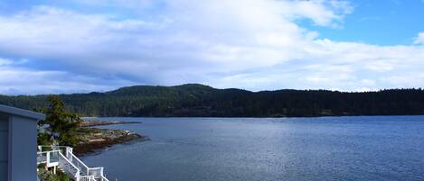 A waterfront property with a staircase leading to a deck, overlooking a calm lake and forested hills.