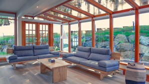 A modern living room with two sofas, a coffee table, and a large window overlooking a garden with rocks and greenery. - Sooke Harbour House (Sooke)