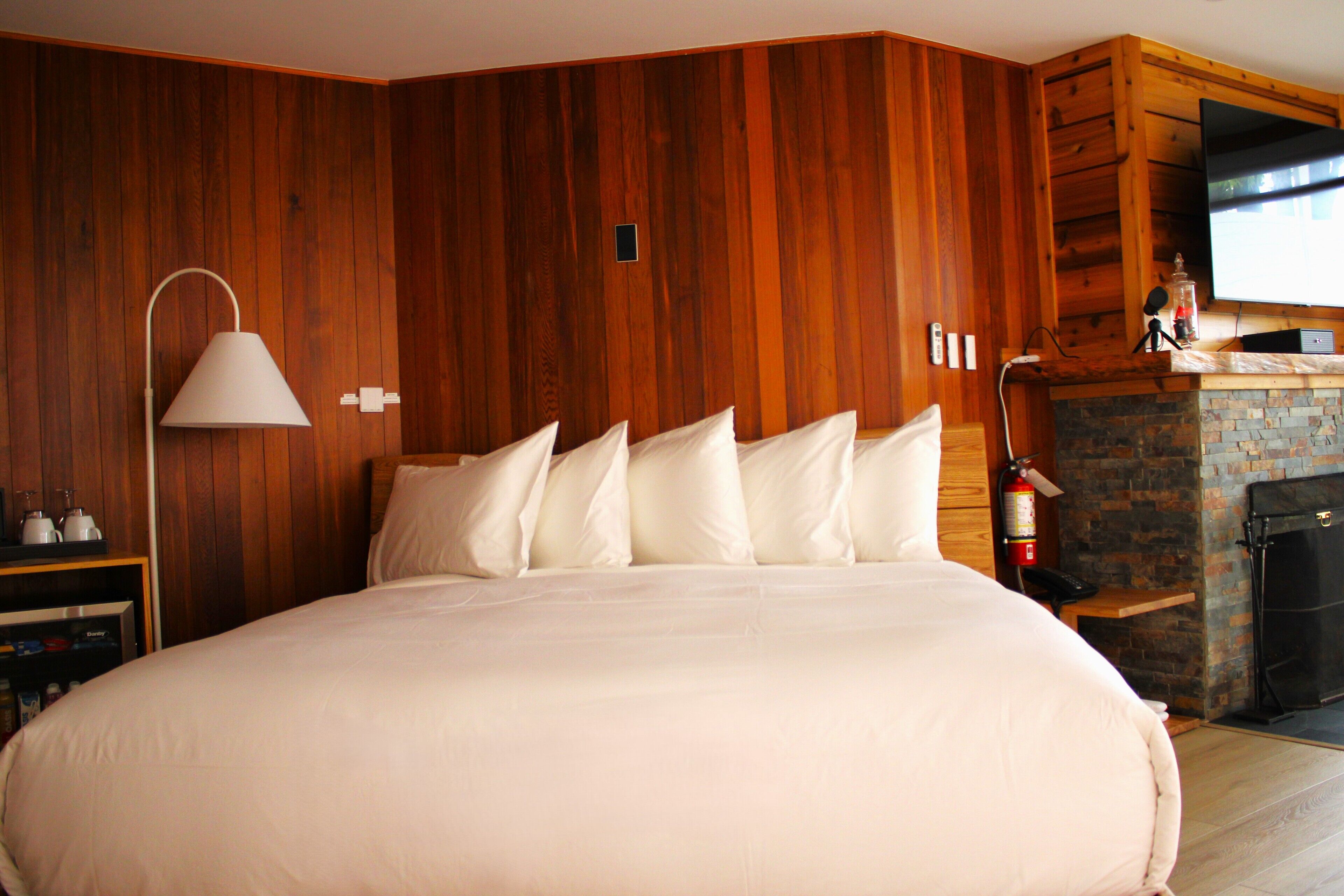 Een groot bed met witte lakens in een kamer met houten lambrisering en een stenen openhaard.