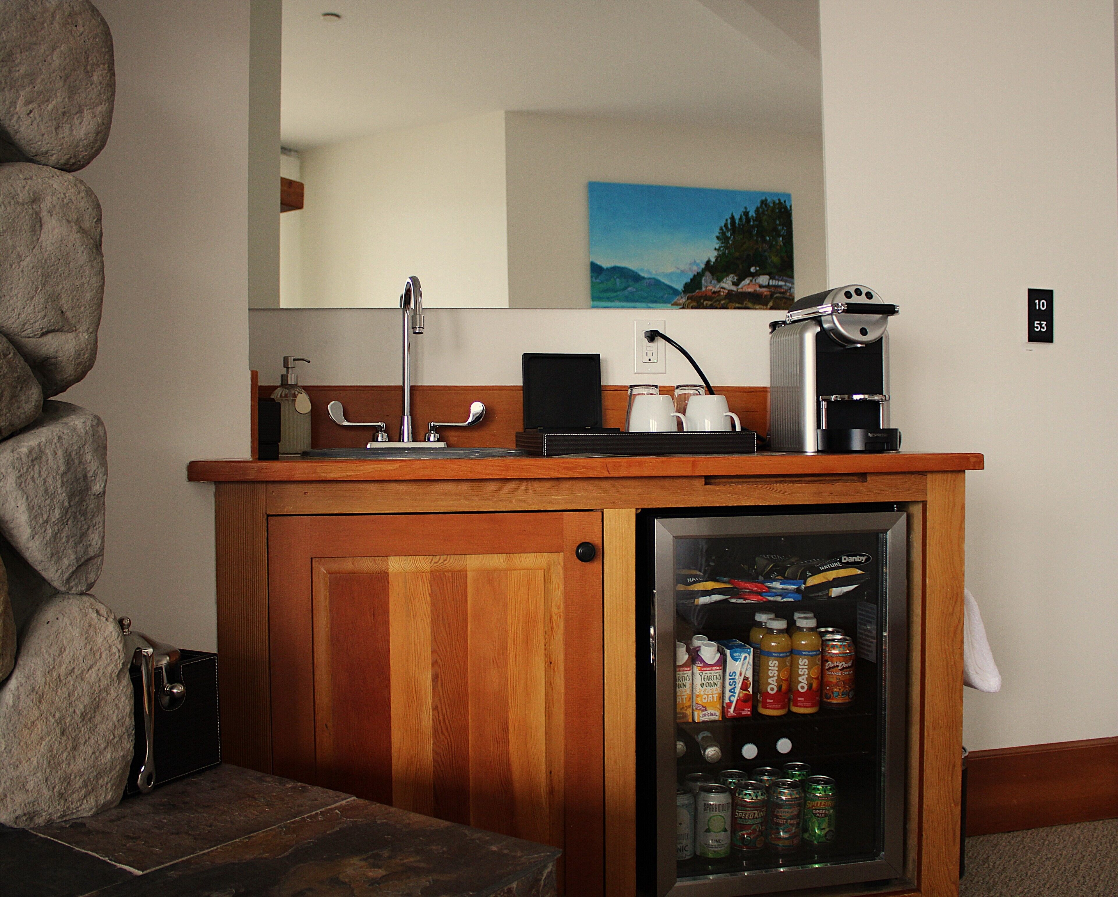 Una encimera de madera con una cafetera y un refrigerador lleno de bebidas.