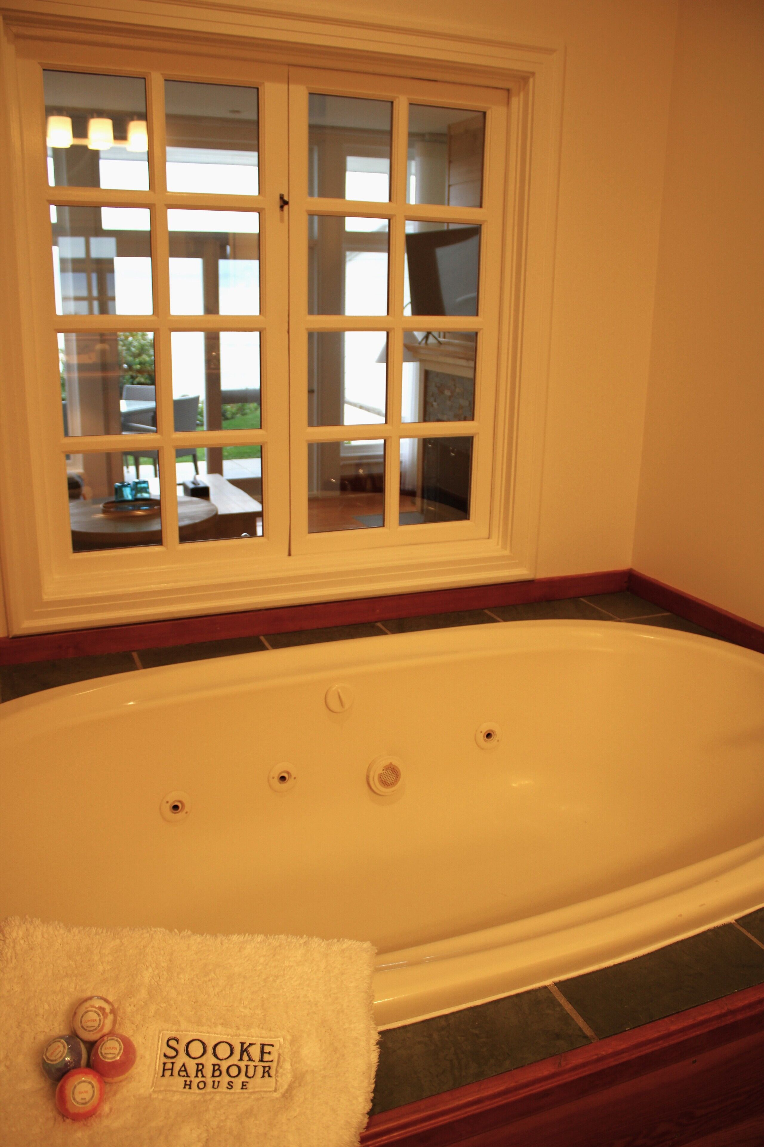 A bathroom with a white bathtub, a window with a view of the outside, and a towel with the text "SOKE HARBOUR HOUSE".