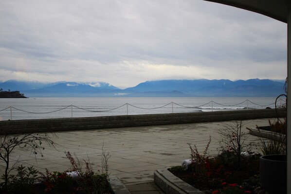 A paved walkway leading to a waterfront with a view of mountains in the distance. - Sooke Harbour House (Sooke)