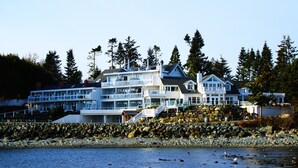 A large, multi-story coastal building with balconies and a stone retaining wall. - Sooke Harbour House (Sooke)
