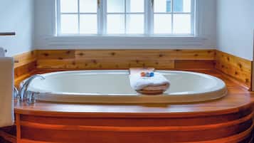 A large, oval-shaped bathtub with a wooden base, positioned under a window with multiple panes.