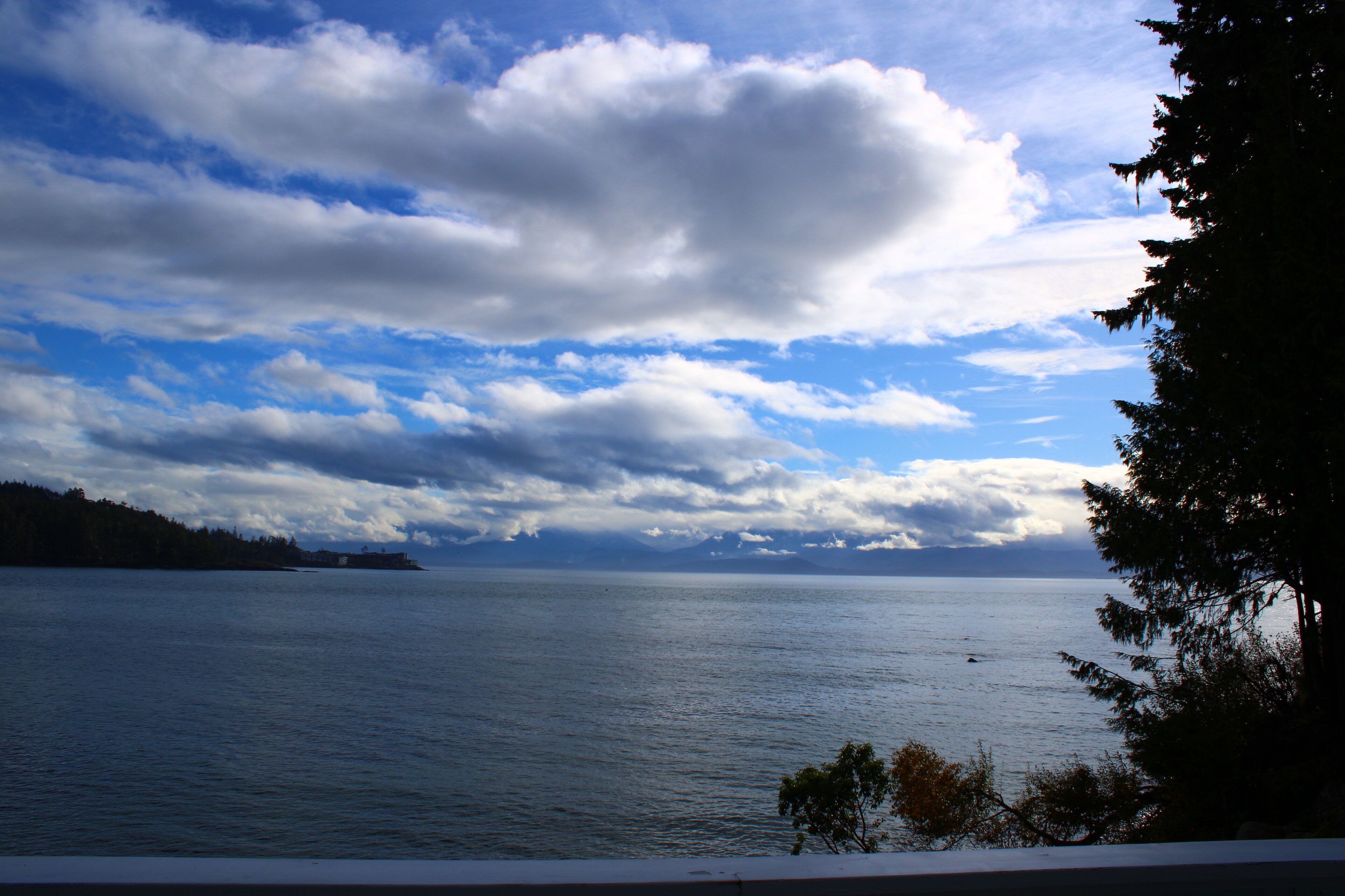 A view of a calm sea with a distant shoreline and a partly cloudy sky.