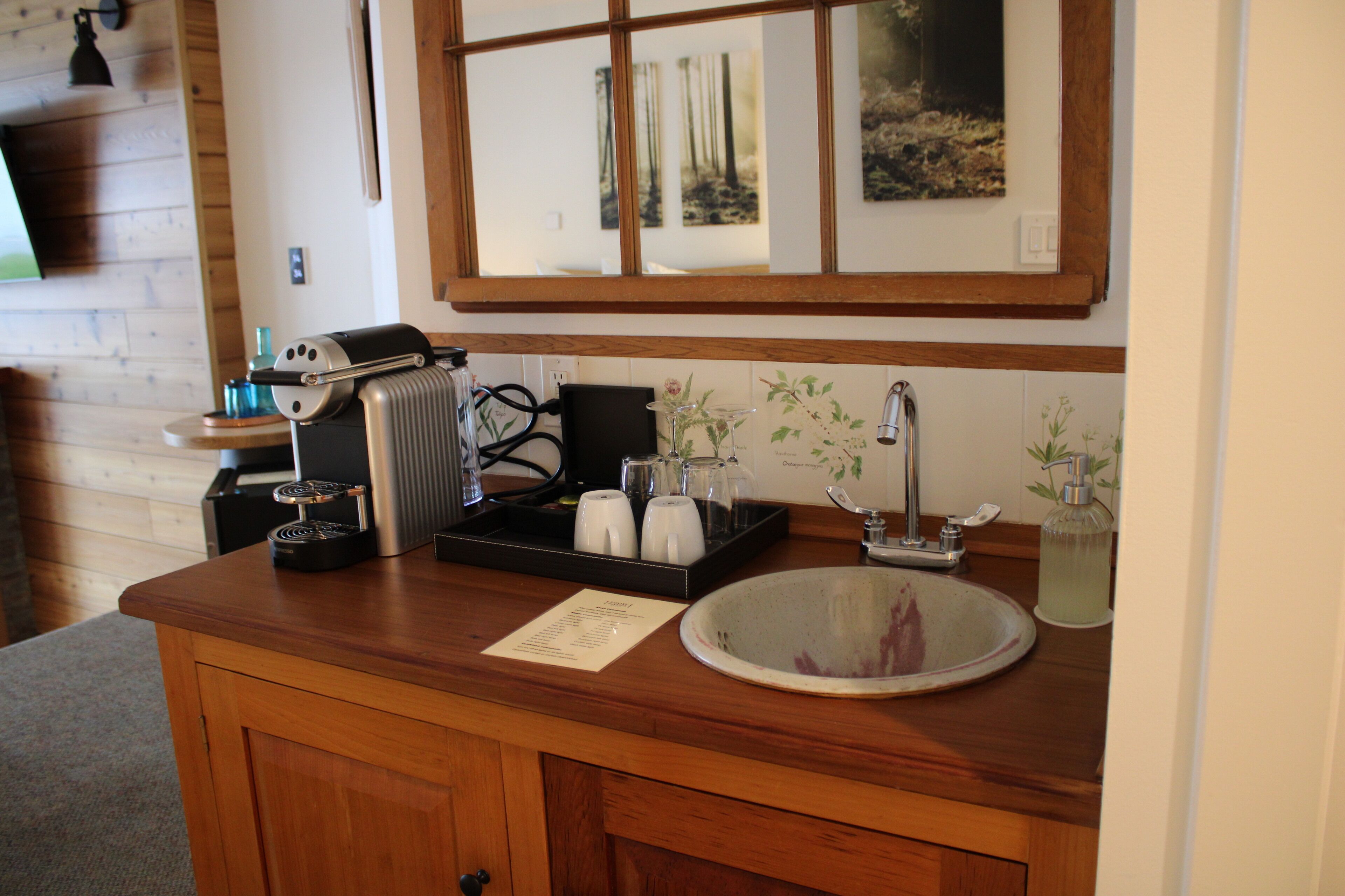 Una encimera de madera en la cocina con un fregadero, una máquina de café y una ventana con una obra de arte encima.