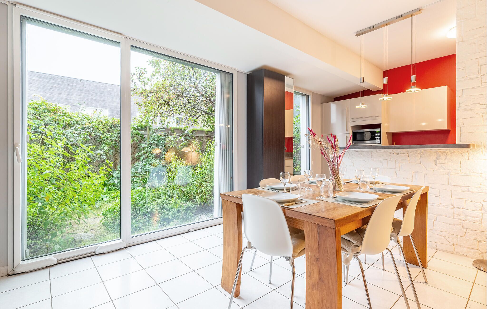 Een eetruimte met een houten tafel voor vier personen, witte stoelen en een uitzicht op een tuin door grote schuifdeuren.