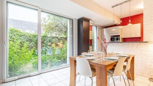 A dining area with a wooden table set for four, white chairs, and a view of a garden through large sliding glass doors.