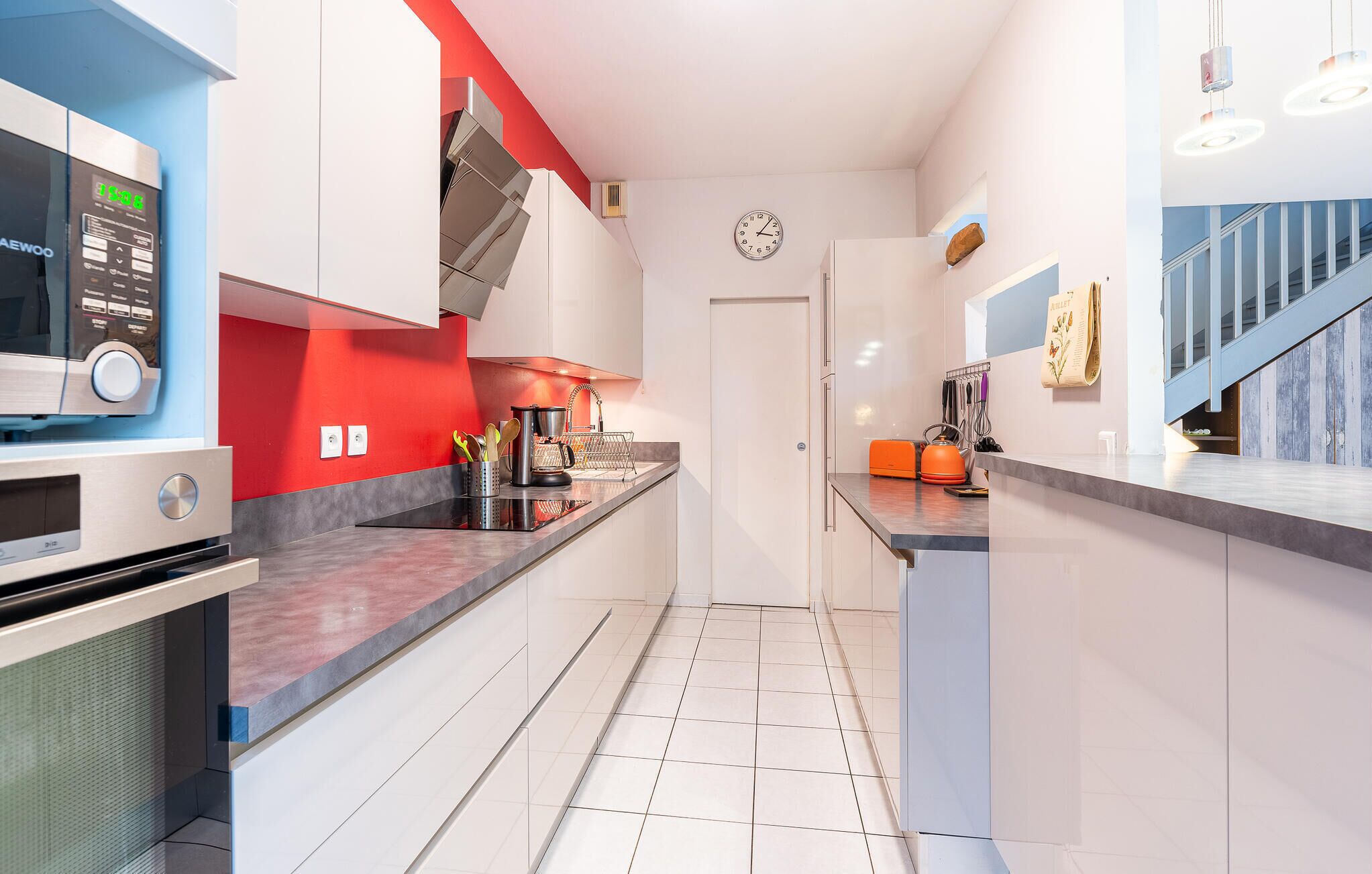 A modern kitchen with stainless steel appliances, a red accent wall, and a visible clock on the wall.