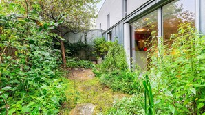 A lush garden with a variety of plants and trees, a small pond, and a building with large windows.