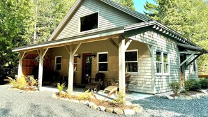 A small, single-story house with a porch, surrounded by trees. - Charming Cottage at Pretty Pond (Mount Desert)
