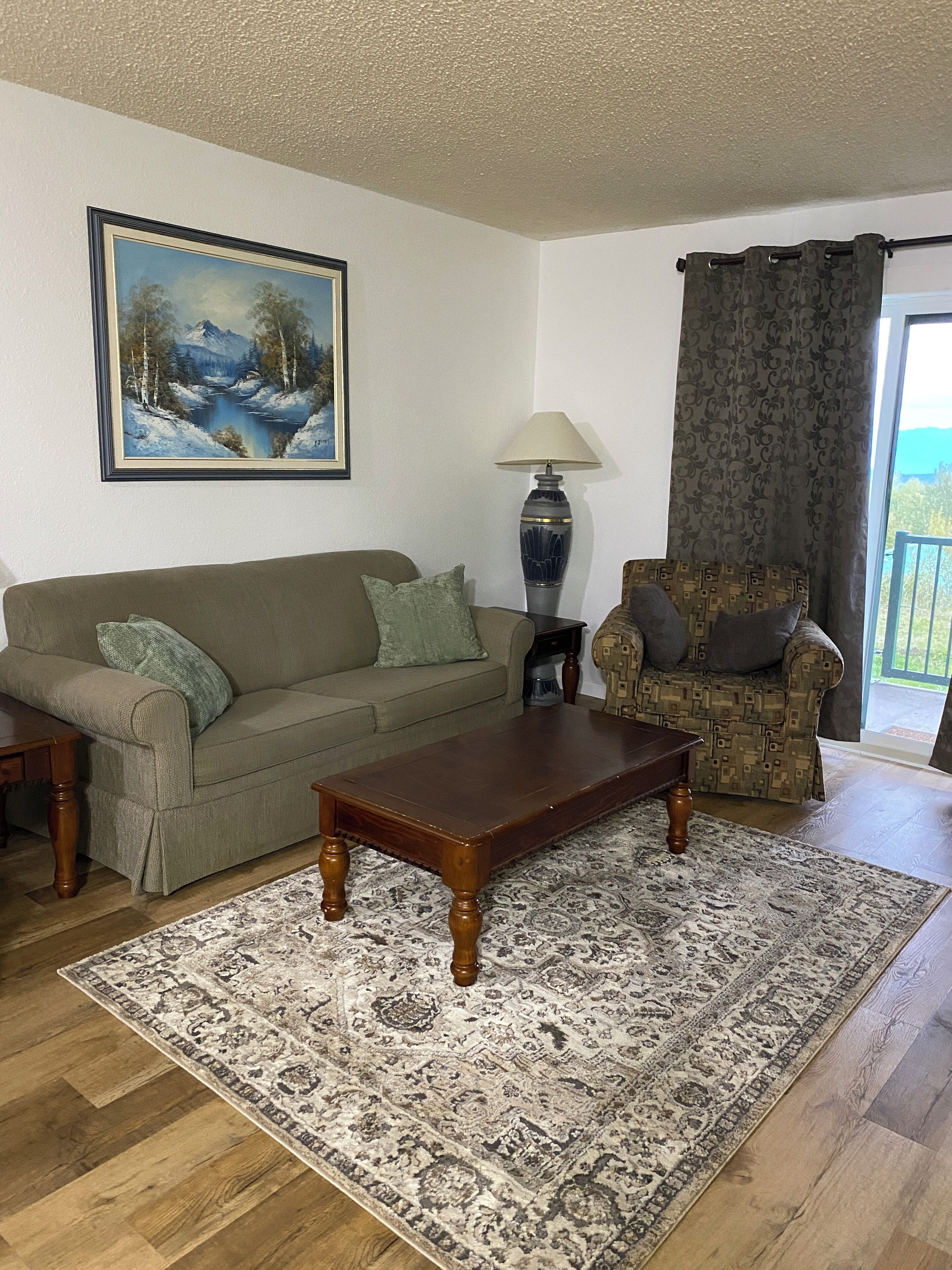 A living room with a sofa, a patterned rug, a coffee table, a lamp, a chair, and a painting on the wall.