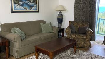 A living room with a sofa, a patterned rug, a coffee table, a lamp, a chair, and a painting on the wall.