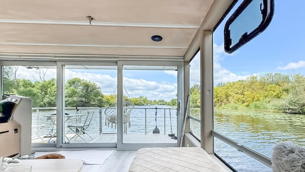 L'intérieur d'un bateau, avec un lit, une table et une vue sur l'eau et la végétation environnante.