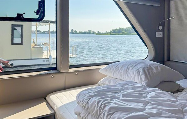 A cabin with a bed, a window overlooking a body of water, and a view of a dock with a boat.