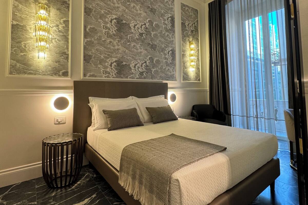 Habitación de hotel moderna con una cama grande, piso de mármol, un muro decorativo con motivos de nubes y vista a la ciudad por la ventana.