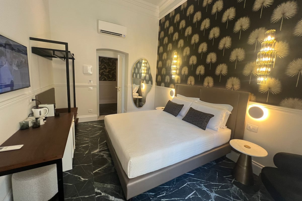 Habitación de hotel con una cama grande, un escritorio con silla, un espejo y aire acondicionado instalado en la pared.