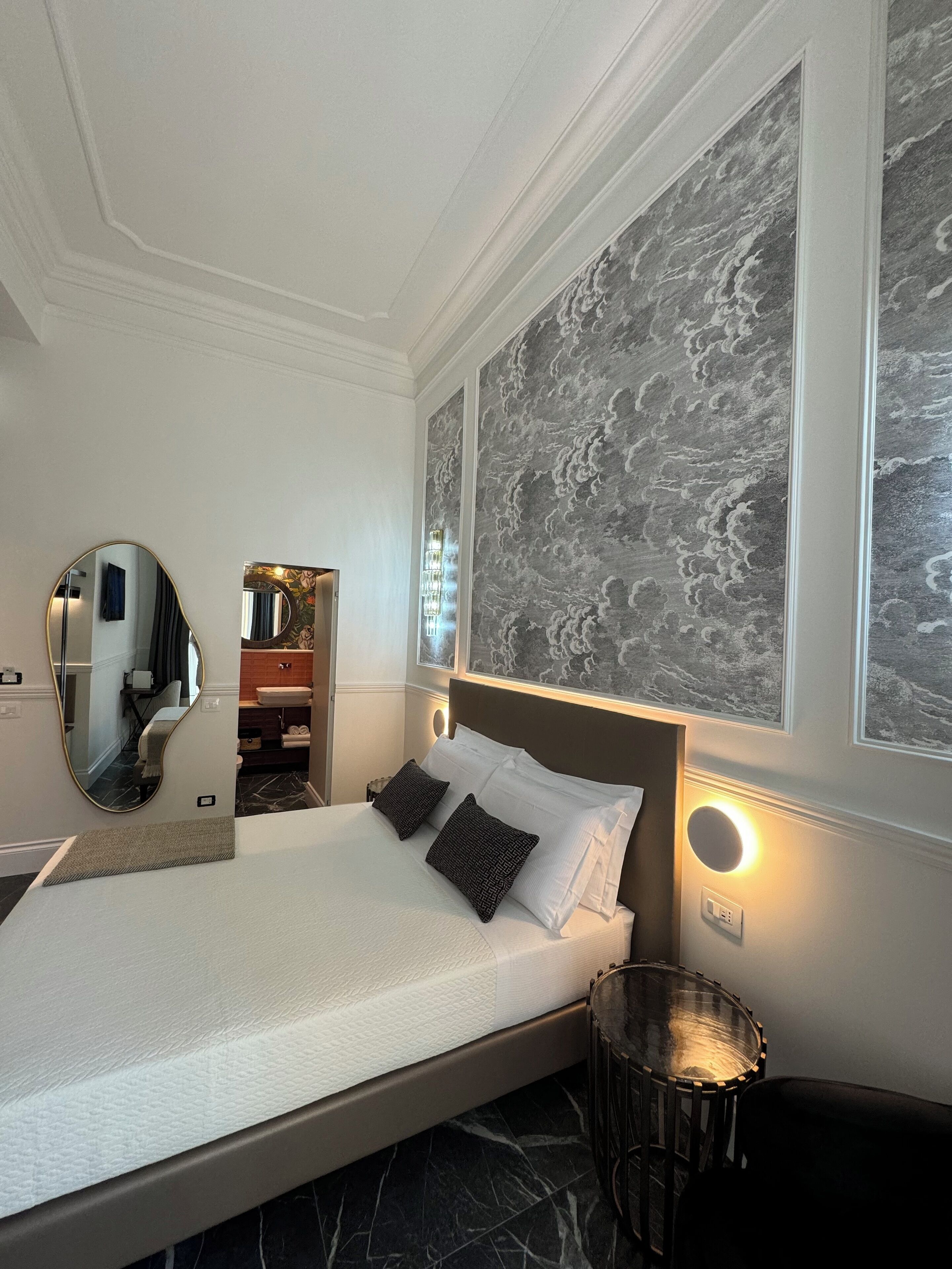 Une chambre moderne avec un grand lit, un miroir rond, une table de chevet et une lampe fixée au mur.