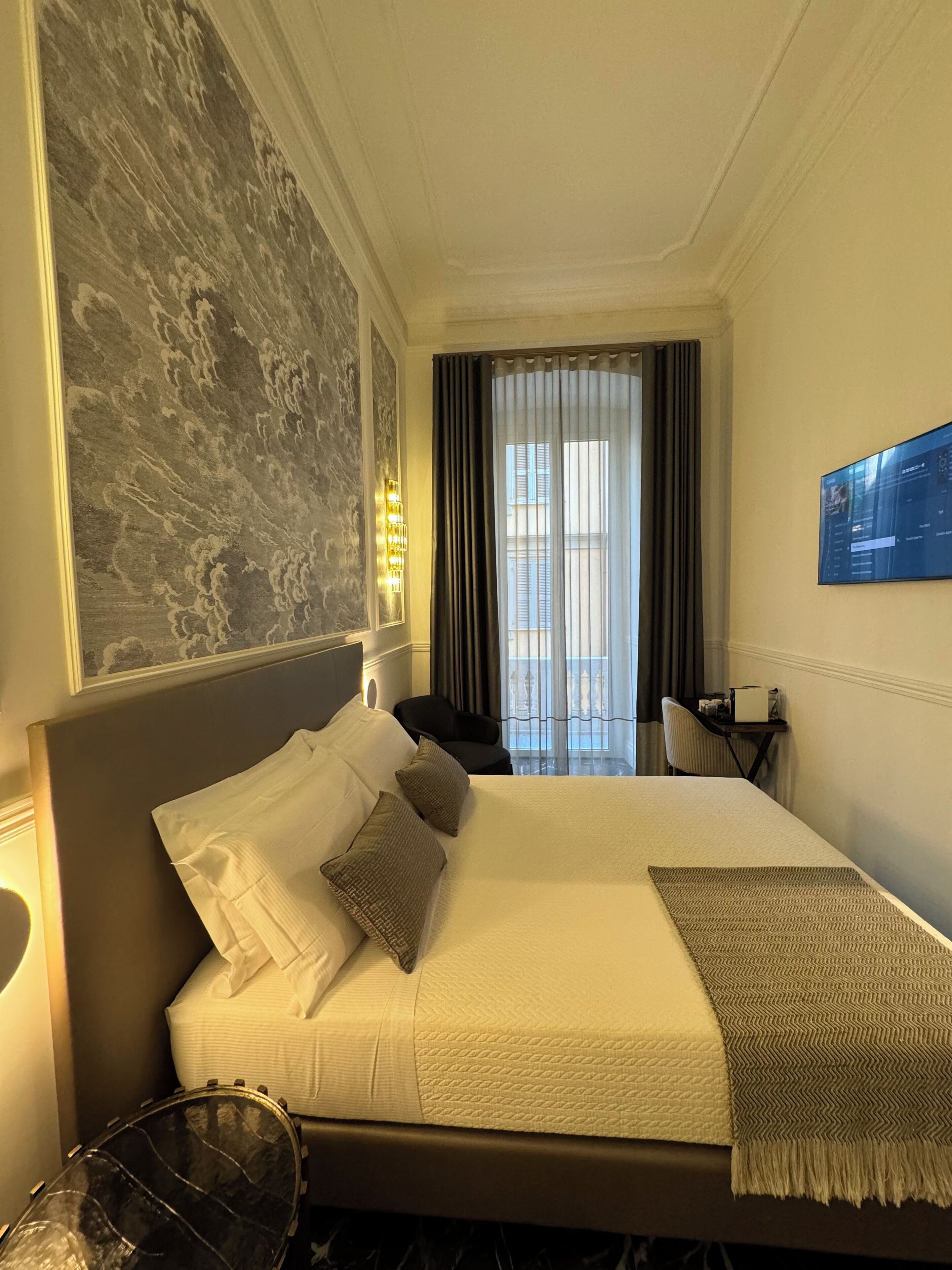 Une chambre d’hôtel avec un grand lit, un bureau, une chaise et un téléviseur fixé au mur.