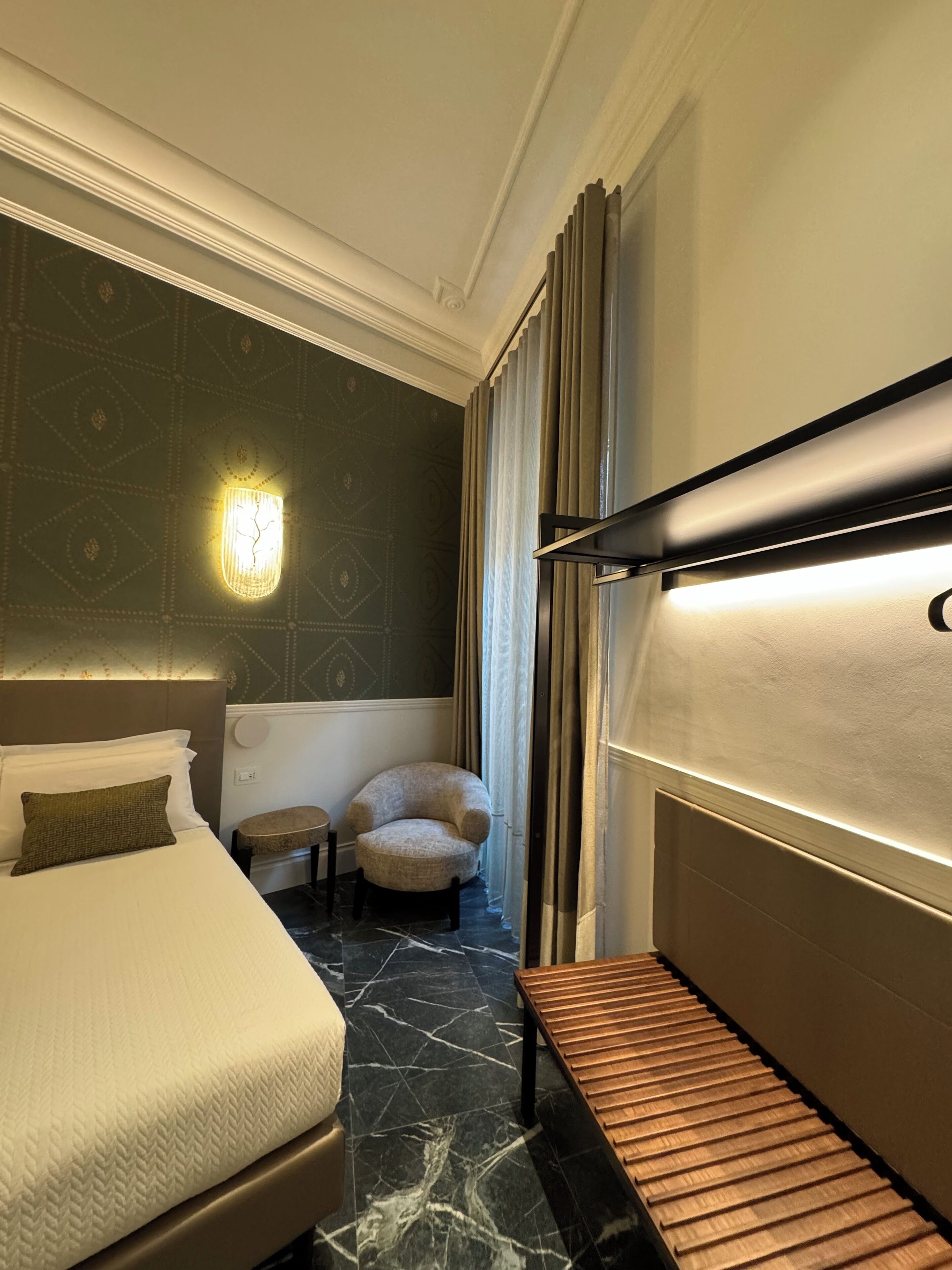 A hotel room with a bed, a chair, a small table, and a bench.