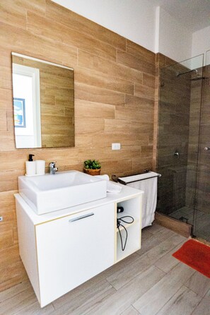 A modern bathroom with a large white sink, a mirror, and a shower area.