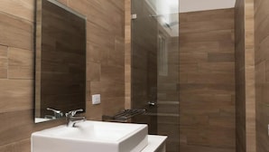 A modern bathroom with a white sink, a glass shower enclosure, and wooden wall tiles. - Baya Azul Bayahibe - Apto 204 (San Rafael del Yuma)
