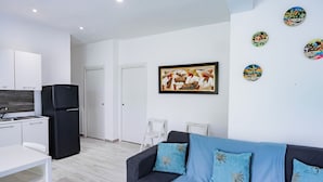 A modern living room with a black sofa, a white dining table, and a black refrigerator. - Baya Azul Bayahibe - Apto 204 (San Rafael del Yuma)